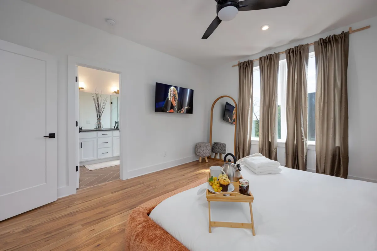 A cozy bedroom with a comfortable bed, TV, breakfast tray, and flowing curtains. The scene evokes lazy mornings, relaxation, and the option to enjoy entertainment or a slow start to the day.