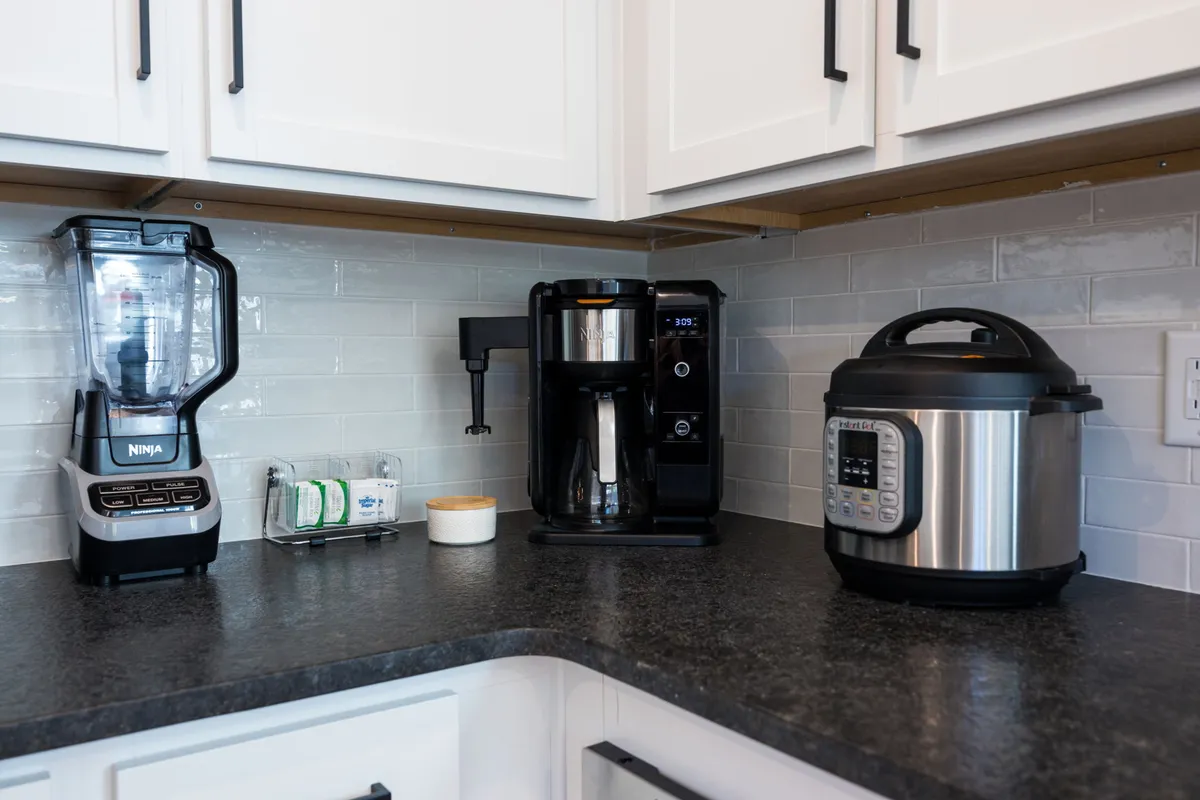 A practical and inviting kitchen countertop scene with a blender, coffee maker, and instant pot, all set against a sleek backdrop. The natural morning light illuminates the countertop, highlighting the convenience of in-unit appliances for meal and beverage preparation.
