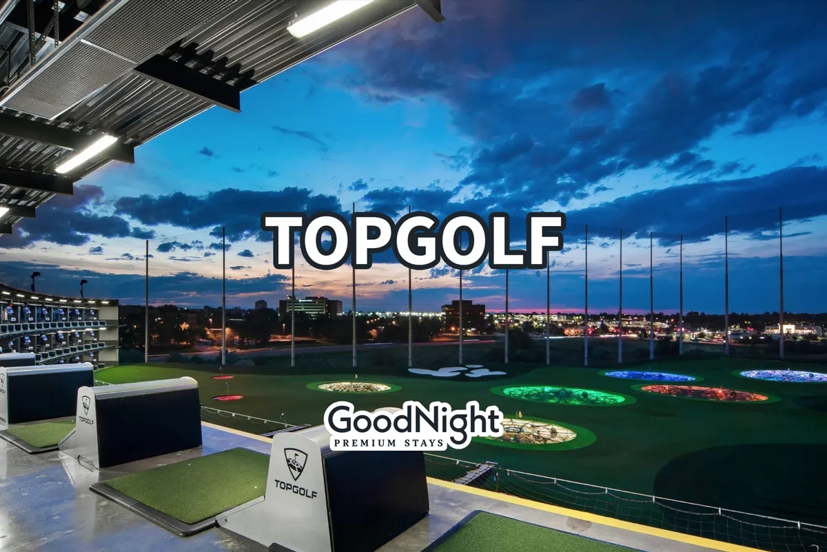 An energetic exterior scene with golf hitting bays, colorful illuminated targets, and a distant city skyline at sunset. People are golfing, dining, and socializing under bistro lights, capturing a festive, group-friendly vibe.