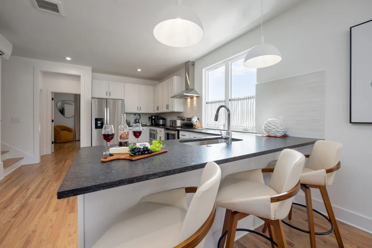 A bright, inviting kitchen scene with a modern island, wine glasses set for a toast, a fruit platter, and a window view providing natural light. The setup suggests a space ideal for cooking, celebrating, and enjoying meals together.