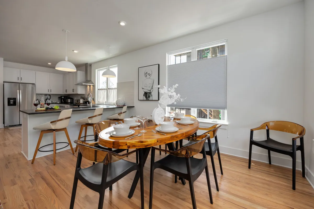 A contemporary dining area featuring a wooden dining table set for a meal, eye-catching artwork on the wall, and an adjacent kitchen island. The atmosphere is welcoming and designed for both intimate dinners and larger gatherings.